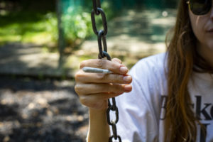 young woman holding a cannabis pre-roll while sitting on a swing